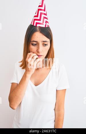 Bella redhead donna che indossa compleanno cappuccio su sfondo isolato cercando stressato e nervoso con le mani sulla bocca di mordere le unghie. Problema d'ansia. Foto Stock