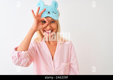 Medioevo donna che indossa blu maschera di sospensione e pigiama isolato su sfondo bianco facendo ok gesto con la mano sorridendo, occhio guardando attraverso le dita wit Foto Stock