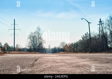 Strada vuota di Chernobyl in Ucraina alberi e pali contro il cielo blu e nuvole Foto Stock