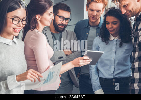 Startupers lavorando insieme a Office in piedi la donna incinta che mostra i colleghi idee sulla tavoletta digitale gioiosa Foto Stock