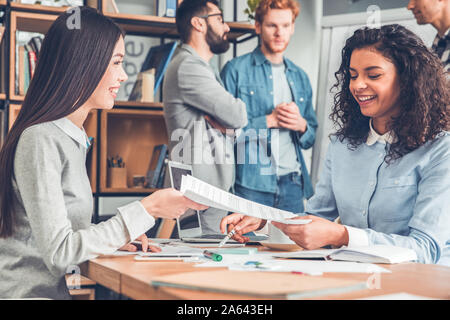 Startupers lavorando insieme a Office donna seduta a tavola passando documenti gioiosa Foto Stock
