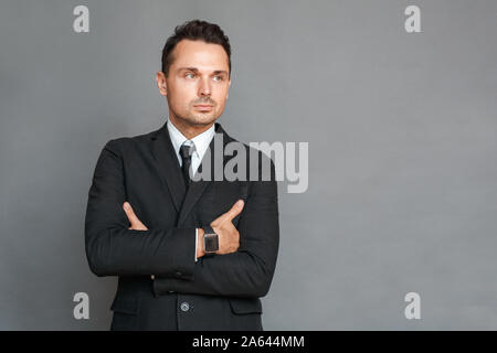 Imprenditore studio isolato permanente su grigio bracci incrociati pensieroso Foto Stock