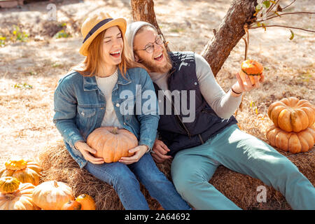 Halloween Preparaton concetto. Coppia giovane seduto in giardino con zucche ridendo allegro Foto Stock