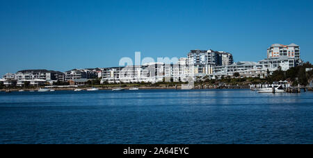 Grandi case di waterside, appartamento condominiums in comunità suburbane sul lungofiume con barche ormeggiate al pontile, cielo blu in background Foto Stock