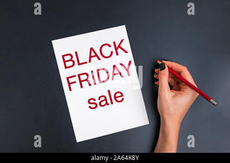 Donna di mano che tiene una matita in prossimità della card con testo nero venerdì Vendita Foto Stock