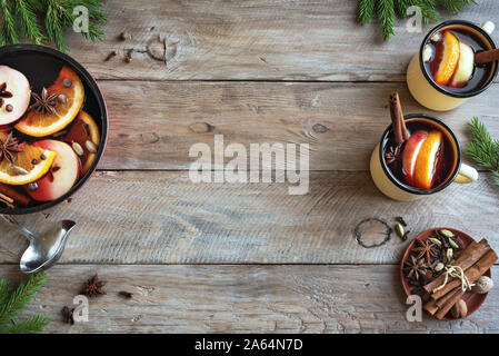 Vin brulé per le vacanze di Natale ed invernali. Vin brulé drink con frutta e spezie in una casseruola e tazze su sfondo di legno, vista dall'alto, copia Foto Stock