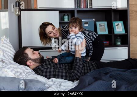 I giovani genitori a giocare con i loro 8 mese-vecchio bambino in letto. Foto Stock