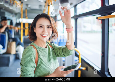 Bella giovane donna asiatica che vedere uno smart phone in città in autobus Foto Stock