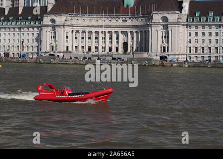 Un rosso motoscafo viaggia a monte sul Fiume Tamigi a Westminster Bridge, Londra, con il Municipio in background e turisti Foto Stock