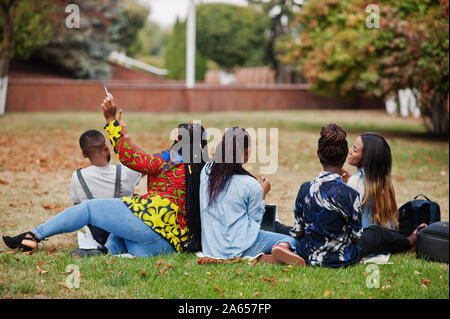 Retro del gruppo africano di cinque studenti del college di trascorrere del tempo insieme sul campus universitario al cantiere. Black afro amici seduti su erba e studiare con Foto Stock