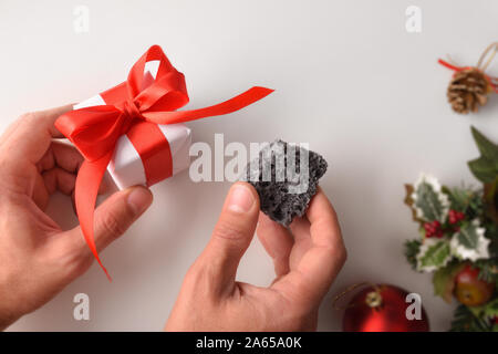 Mani con il dono e il carbone il giorno di Natale. Il concetto di ricompensa per il buono o cattivo comportamento. Composizione orizzontale. Vista dall'alto. Foto Stock