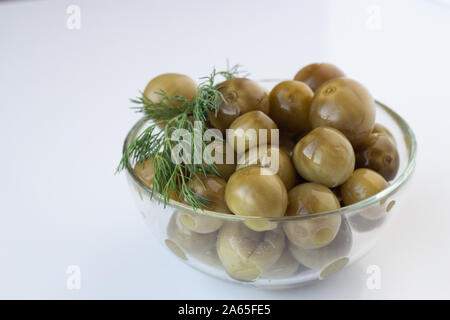 Sour green pomodorini con aneto in una lastra di vetro su uno sfondo bianco Foto Stock