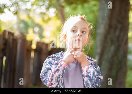 Una bellissima bambina cercando curiosamente in distanza in estate foresta. Foto Stock