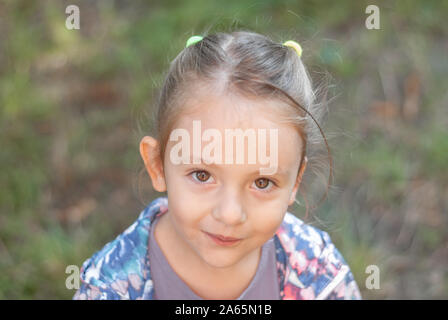 Una bellissima bambina cercando curiosamente in distanza in estate foresta. Foto Stock