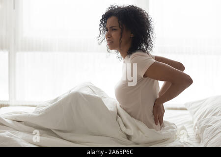 Uno stato di malessere nero ragazza sveglia in camera da letto con un mal di schiena Foto Stock