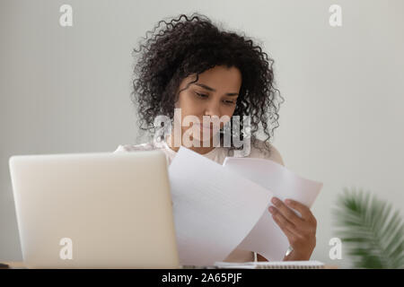 Concentrato nero ragazza di leggere la documentazione lo studio sul computer portatile Foto Stock