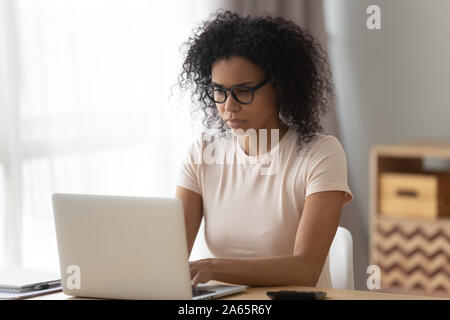 Concentrato nero donna in bicchieri occupato a lavorare al computer portatile Foto Stock