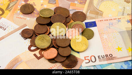 Una pila di monete in euro su un letto di cinquanta e venti euro bills Foto Stock