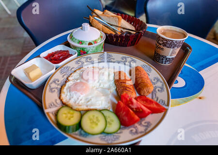 Inglese tradizionale succulenta prima colazione con uova salsicce Pomodori Cetrioli e una tazza di caffè Foto Stock