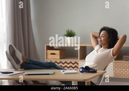 Felice nero donna rilassarvi in poltrona alla scrivania a casa Foto Stock