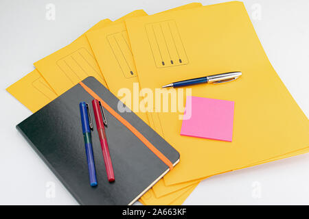 Forniture per ufficio costituito da marcatore fluorescente, il rosso e il blu marcatori, penna moderna, blocco note appiccicose e note book su giallo sottocartelle Foto Stock