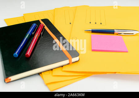 Forniture per ufficio costituito da marcatore fluorescente, il rosso e il blu marcatori, penna moderna, blocco note appiccicose e note book su giallo sottocartelle Foto Stock
