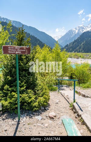 Esik lago Issyk pittoresca vista mozzafiato con il cartello stradale che conduce al sito e delle montagne innevate su una soleggiata cielo blu giorno Foto Stock