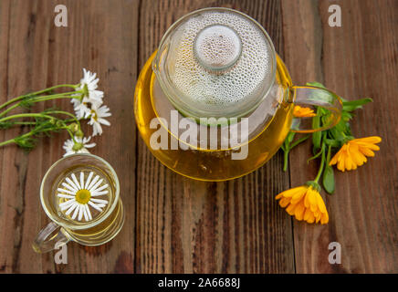 Teiera trasparente e la coppa con tè alle erbe e fiori su sfondo di legno. Foto Stock