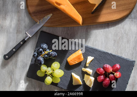 Selezione di formaggi serviti con rosso e bianco di uve nere. Flatlay snack food immagine. Leicester cheddar e formaggi a pasta dura con frutta servita su legno e sl Foto Stock