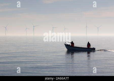 Sostenibile delle risorse stile di vita alternativo. Piccola barca da pesca con sulle turbine eoliche offshore. Calma foschia mattutina. Due pescatori di uscire in mare. Tra Foto Stock