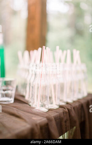 Bottiglie per la limonata sul tavolo in legno all'esterno. Set di bottiglie in vetro per la limonata e cocktail. Catering, ricevimento di nozze concetto. Foto Stock