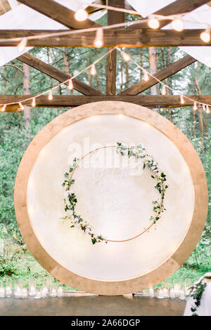 Nozze arco tondo in stile rustico decorato con ghirlande di fiori e vegetazione, retro lampadine sul soffitto. Bellissimo matrimonio istituito. Area Foto Stock