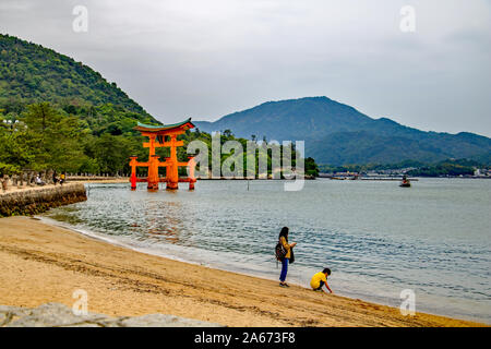Una madre e figlio sulla spiaggia presso l'isola di Miyajima, Giappone con le floating gate torii in background Foto Stock