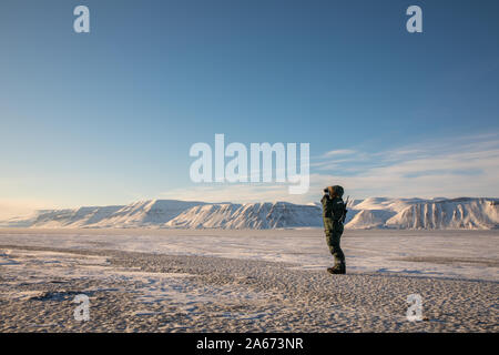 Uomo con un fucile e binocoli si affaccia sull'orizzonte nel paesaggio artico a Svalbard Foto Stock