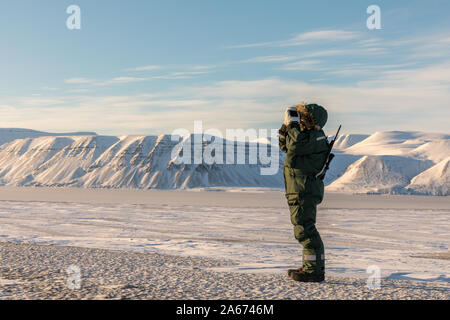 Uomo con un fucile e binocoli si affaccia sull'orizzonte nel paesaggio artico a Svalbard Foto Stock