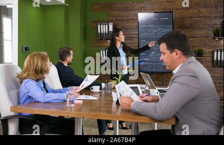 Imprenditore nel soddisfare ascoltando la sua collega presentando grafici su schermo tv nella sala conferenze. Foto Stock