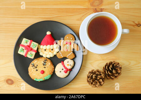 Vista dall'alto di una piastra di biscotti di Natale con una tazza di tè caldo servito su un tavolo di legno Foto Stock