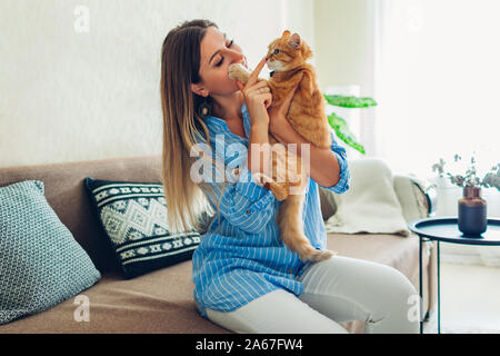 Giocando con il gatto di casa. Felice giovane donna seduta sul lettino teasing e abbracciando il pet. Sensazione accogliente speding tempo con lo zenzero gattino Foto Stock