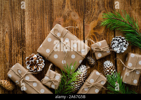 Regalo di natale scatole avvolte in una carta craft, coni e rami di abete su legno sfondo rustico. Piatto, laici overhead e spazio per il testo. Foto Stock