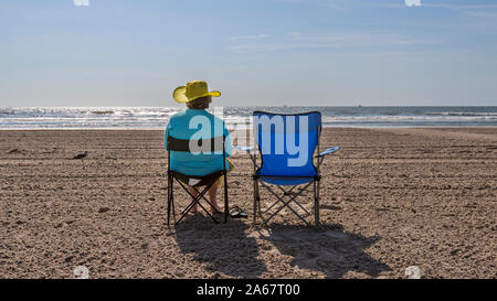 Un senior donna godendo seduto in una sedia spiaggia in sabbia sulla spiaggia dalla Ocean Shore. Foto Stock