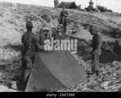 Un gruppo di soldati americani, fuori in una giornata di sole, preparando un campo su una collina aperta, Vietnam, 1965. () Foto Stock