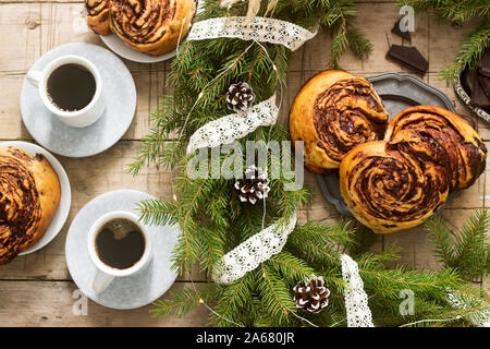 Lumaca muffin al cioccolato servito con il caffè sullo sfondo di una ghirlanda di rami di abete e coni. Stile rustico. Foto Stock