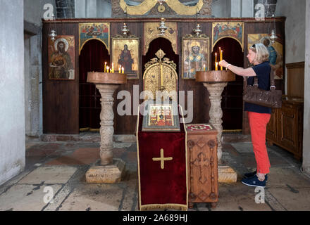 Una touring donna accende una candela in Saint Nicholas Chiesa serbo-ortodossa di Kotor, Montenegro. Foto Stock