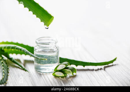 Fresh Aloe foglie e il vasetto di vetro di aloe vera succo di colore bianco su sfondo di legno. La medicina naturale concetto. Foto Stock