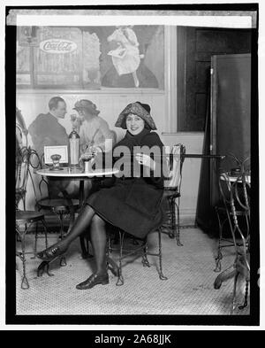 Donna seduta a una fontana di soda tabella viene colata di alcol in una tazza da una canna, durante il proibizionismo; con una grande pubblicità Coca-Cola sulla parete], 2/13/22 Foto Stock