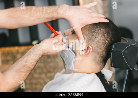 Parrucchiere rade la barba di un uomo con un rasoio in un barbiere Foto Stock