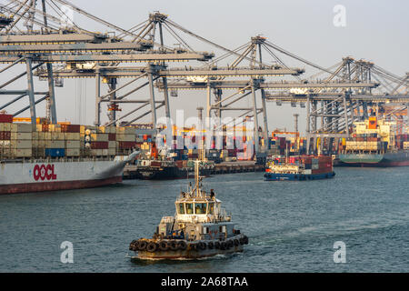 Il Porto di Laem Chabang seaport, Tailandia - 17 Marzo 2019: le righe del contenitore grigio gru, colorato di pile di scatole, e una linea di navi portacontainer con uno tugbo Foto Stock