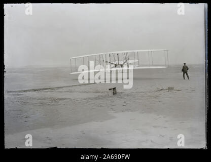 Primo volo, 120 metri in 12 secondi, 10:35 del mattino; Kitty Hawk, North Carolina (restaurata foto); altri primo volo, Dicembre 17, 1903 restaurato (foto); riepilogo: il primo powered, controllato e sostenuto il volo aereo nella storia. Orville Wright, età 32, è ai comandi della macchina, che giace prono sulla aletta inferiore con fianchi in culla che gestiva l'ala-meccanismo di orditura. Suo fratello Wilbur Wright, età 36, corse a fianco per aiutare a bilanciare la macchina, avendo appena rilasciato la sua presa sul montante in avanti del parafango destro. La rampa di partenza, l'ala-resto, una bobina box, e altri elementi ne Foto Stock