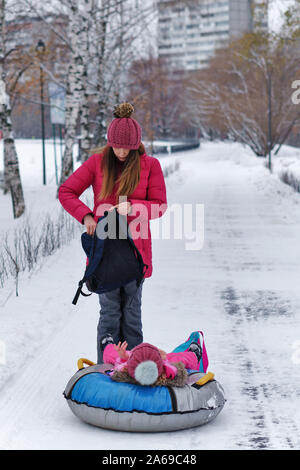 Attivo giovane madre rotoli il suo bambino su un snow tubing. Attività invernali. La Felicità di essere un genitore. Aspetto familiare. Foto Stock