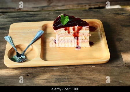 Torta di velluto con frullato di fragola e sciroppo rosso, cibo dolce con cucchiaio e forchetta sul piatto di legno marrone con la tabella in background Foto Stock